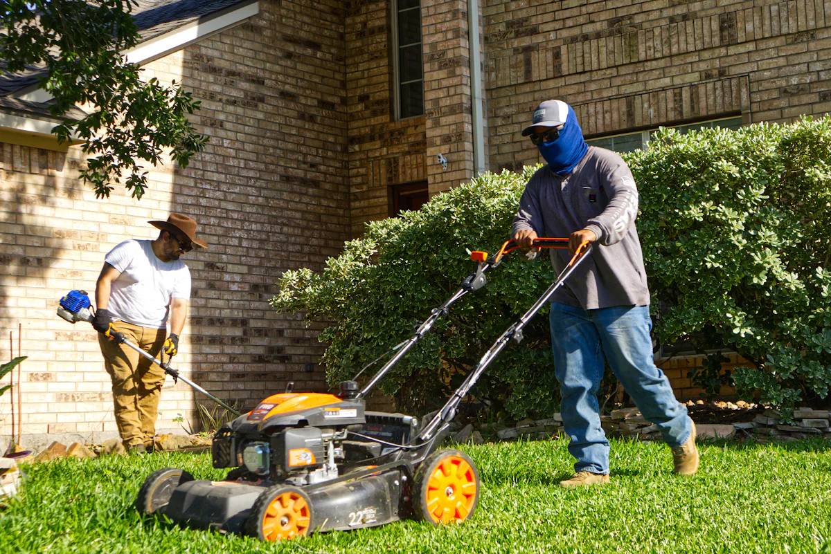 A two-person lawn crew mowing and trimming a residential yard